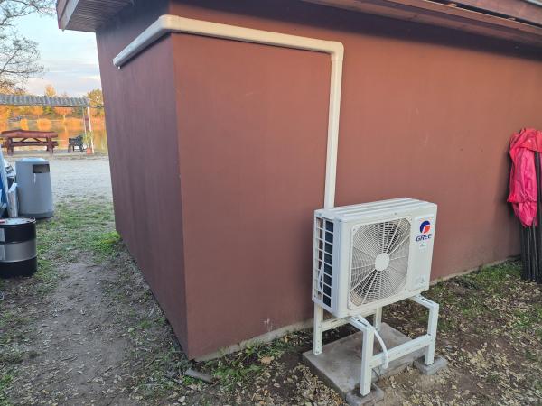Gree kültéri egység földre állított tartókereten, egy épület hátsó falánál – klímaszerelés, Balázs Klíma